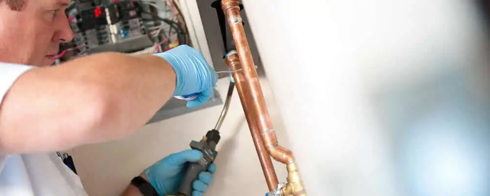 Water heater repair technician testing copper pipe connections and controls in West Palm Beach, FL